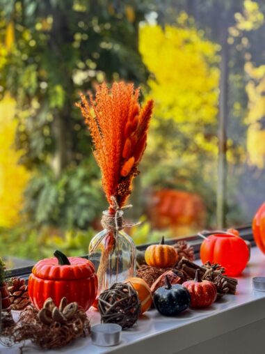 Herbstdekoration mit Kürbissen und Trockenblumen am Fenster