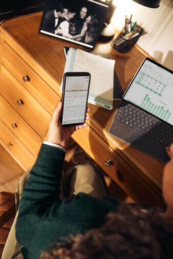 Person nutzt Smartphone neben Laptop und Tablet am Schreibtisch