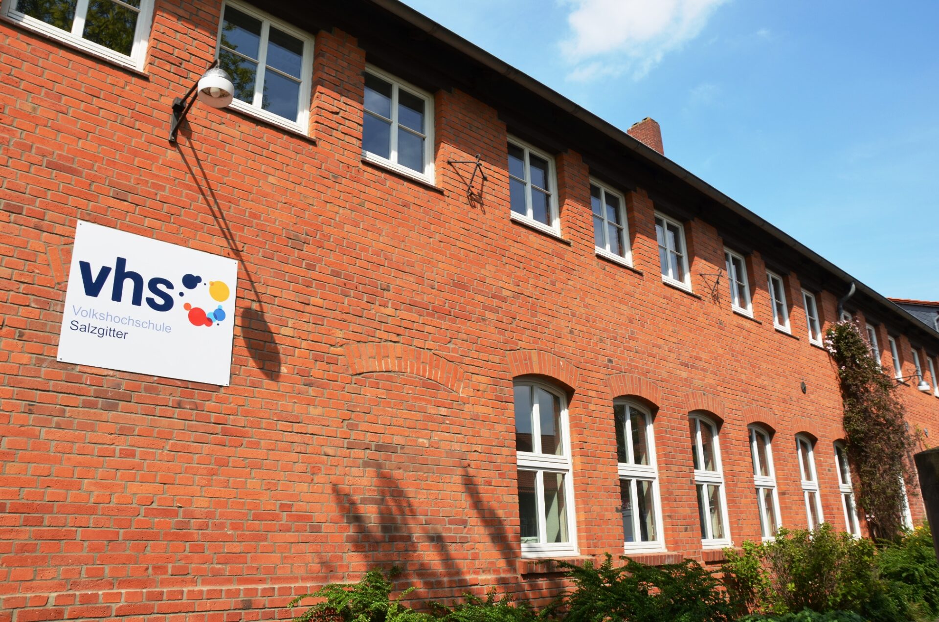Rote Backsteinfassade der Volkshochschule Salzgitter mit vhs-Schild und weißen Fenstern.