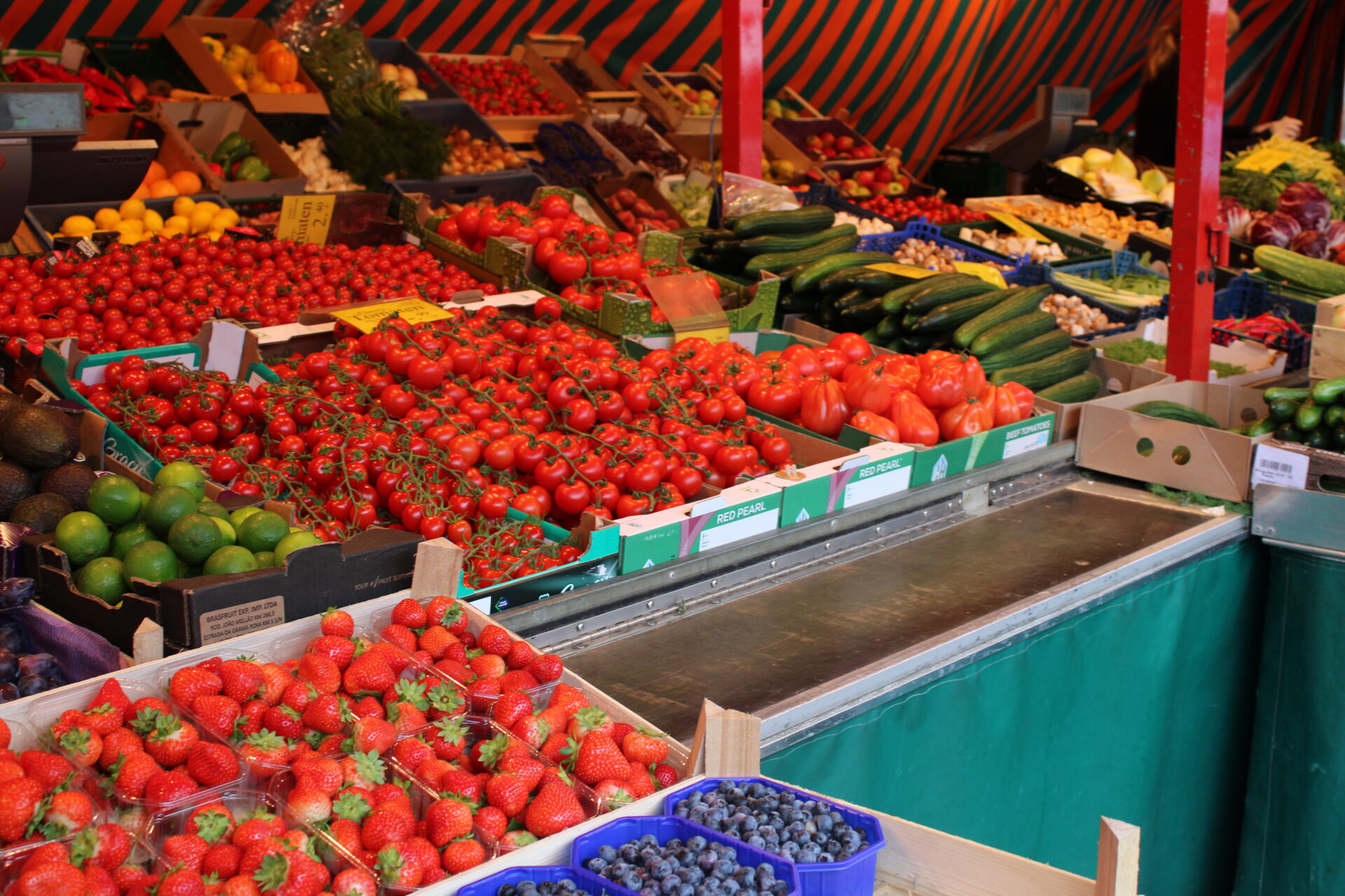 Marktstand mit großer Auswahl an frischem Obst und Gemüse wie Erdbeeren, Tomaten und Gurken.